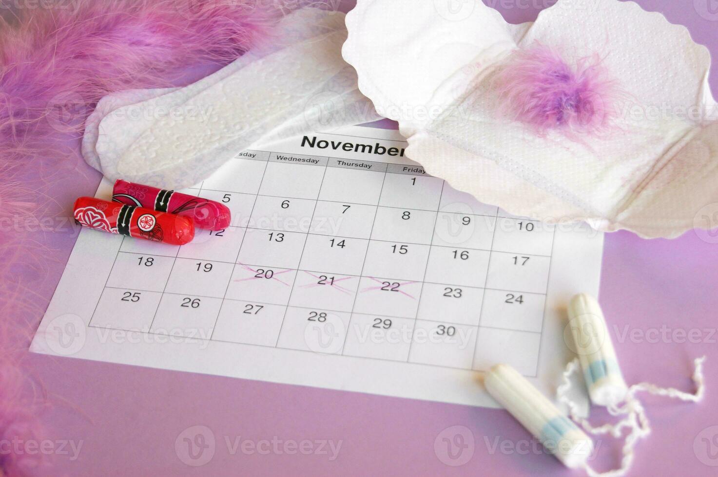 Menstrual pads and tampons on menstruation period calendar with on lilac background. photo