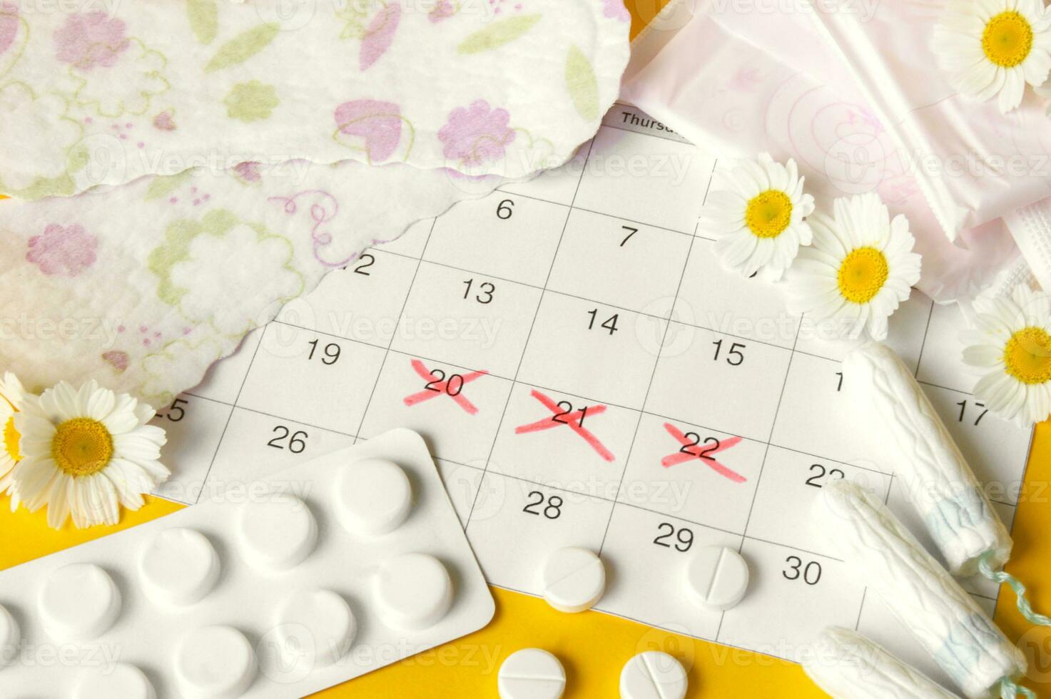 Menstrual pads and tampons on menstruation period calendar with chamomiles on yellow background. photo