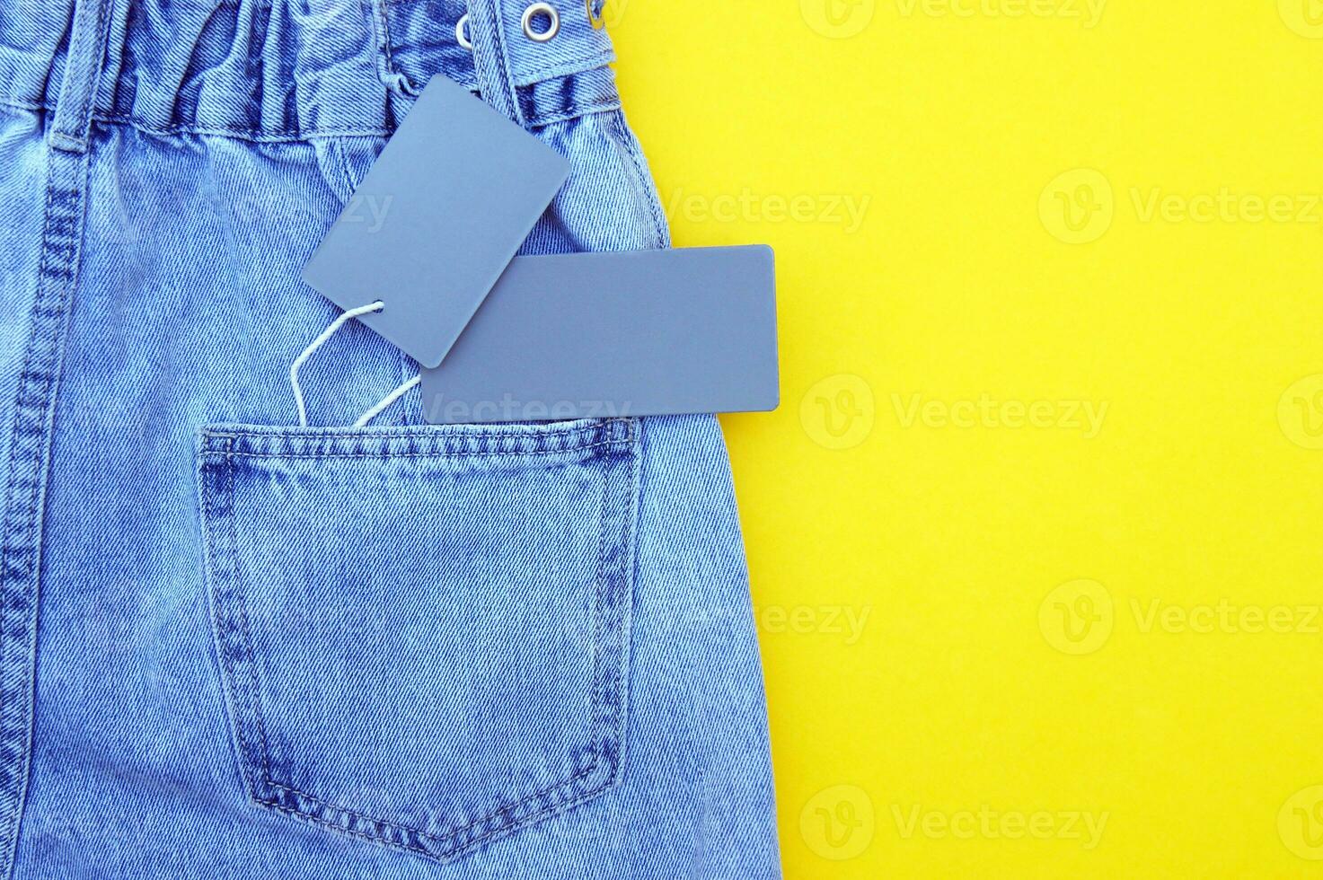 Flat lay, detail of blue jeans with blank gray label on yellow background. photo