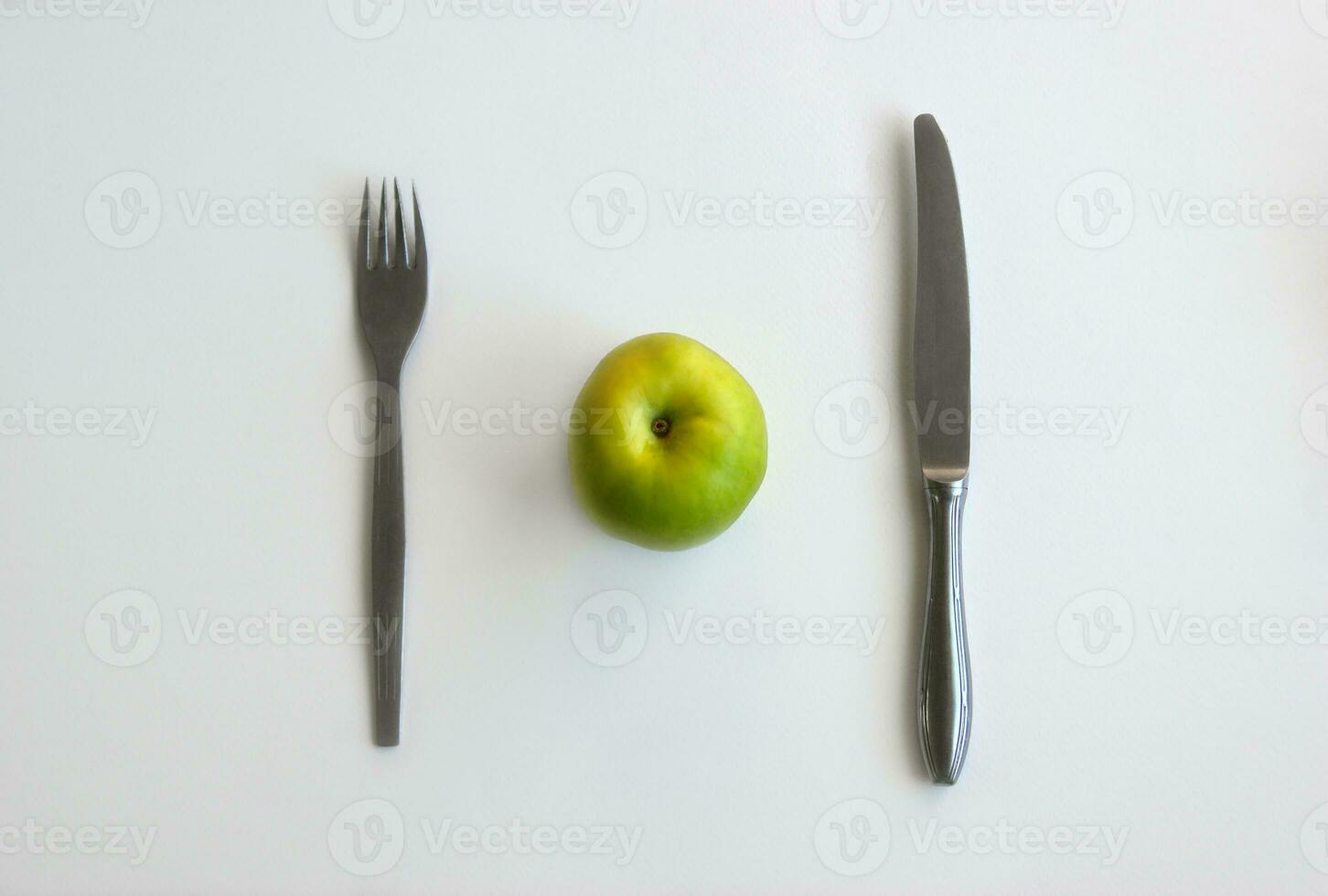 Green apple with knife and fork on white background top view photo