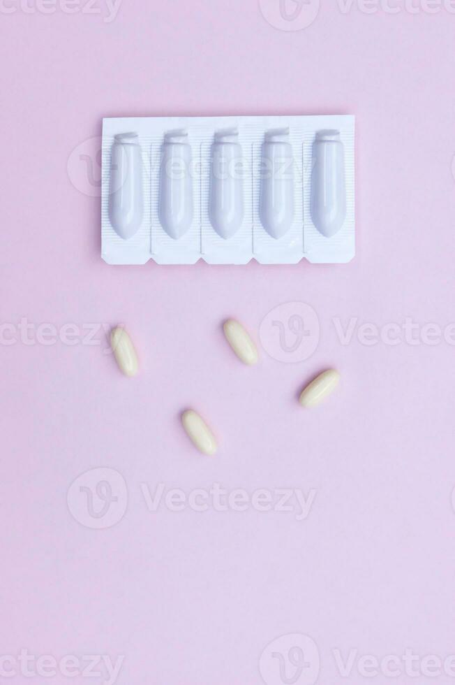Gynecological medicines for women's health in form of suppository, capsules on pink background. photo