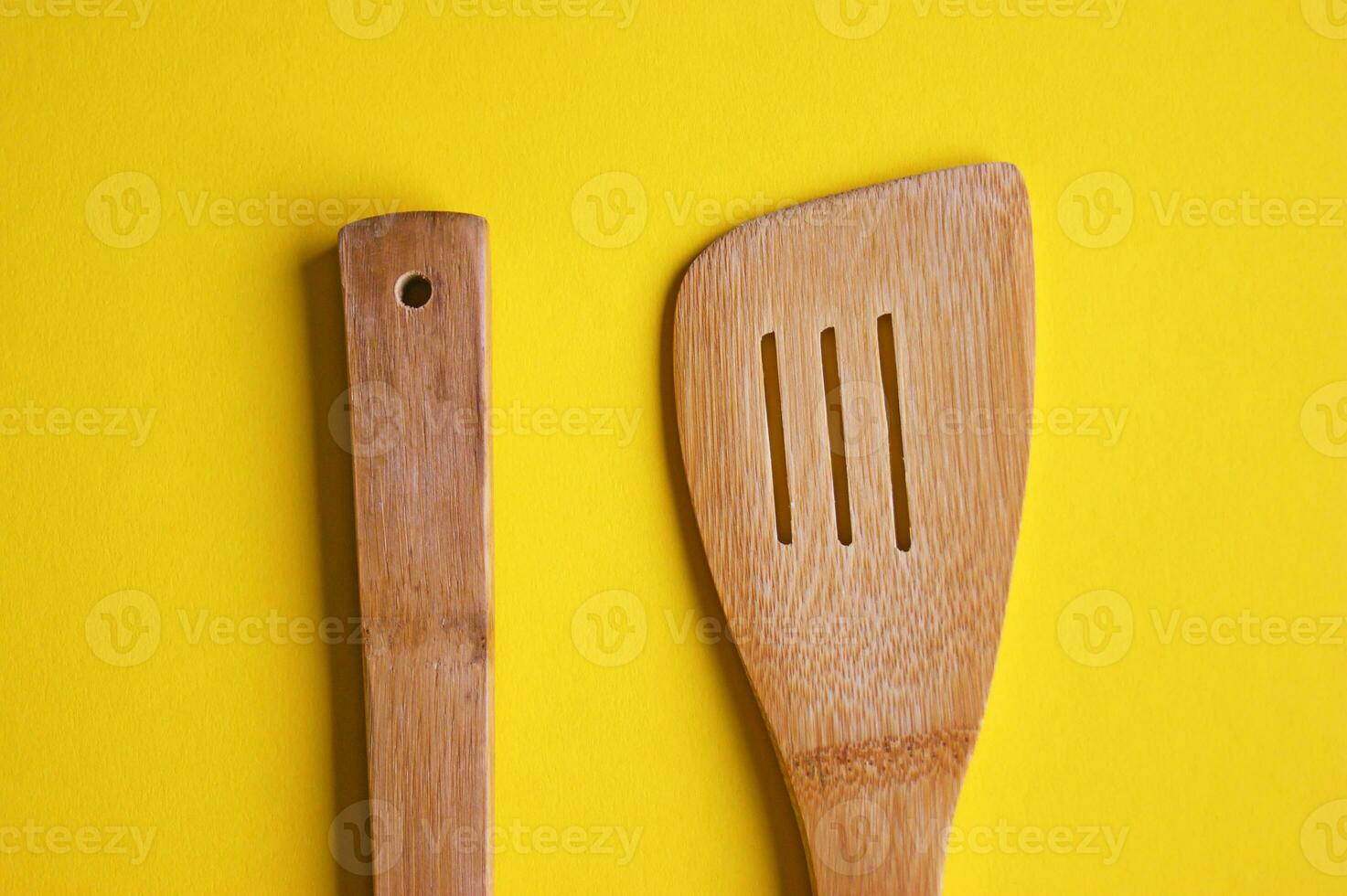 Top view of wooden kitchen spoon and spatula isolated on yellow background. photo