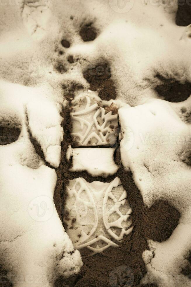 Big boot footprint in fresh wet snow on brown clay like mud in sepia photo