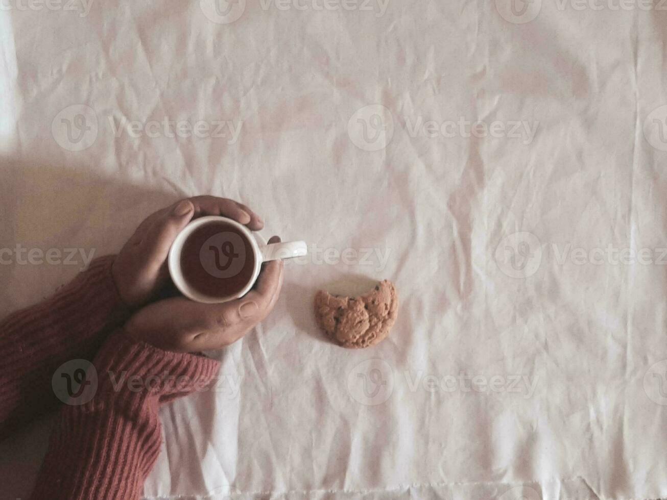 hand holding tea cup, cookie on table, cozy hugge concept. Pastel colors, warm sweater, vintage style. High quality photo. photo