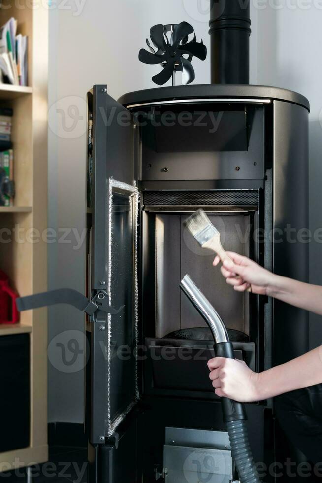 Woman cleaning pellet stove with accessoiries as vacuum cleaner or brush photo