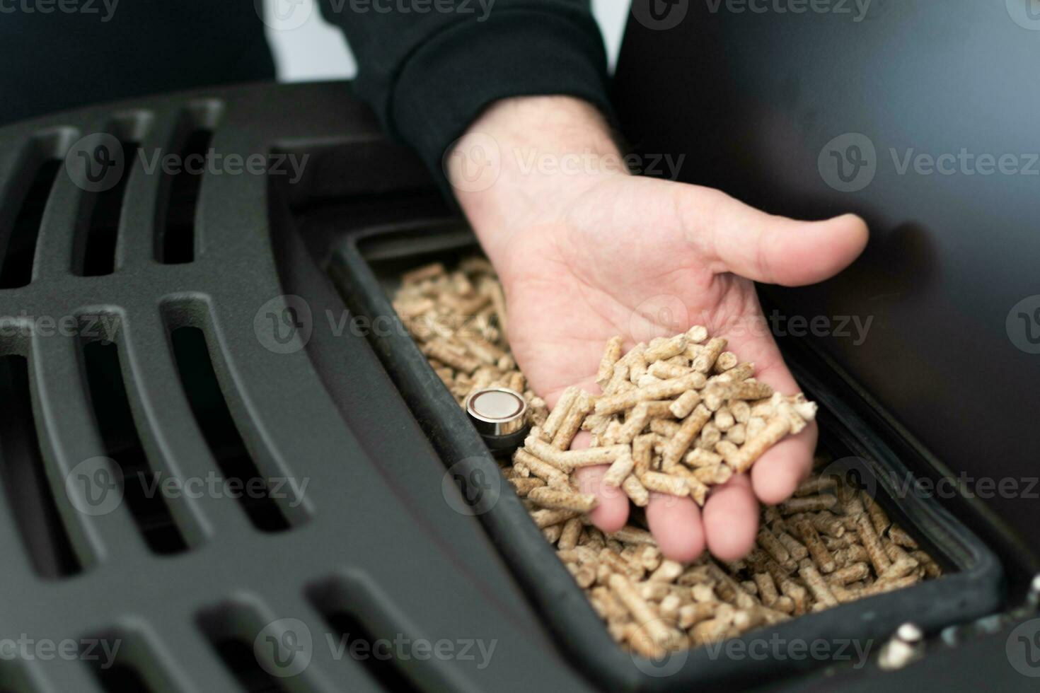 Pellet stove, man holding granules in his hand above a modern black stove photo