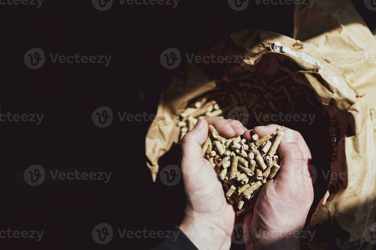 Man's hands holding fir pellet above a kraft bag photo