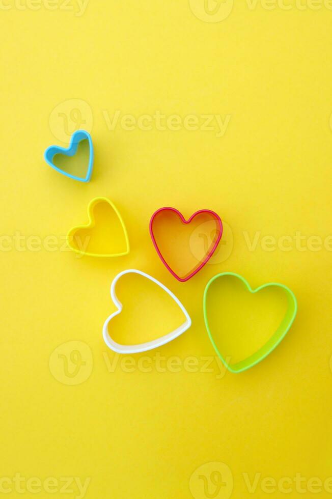 Plastic molds of multi colors for making cookies in the shape of a hearts on a yellow background. photo