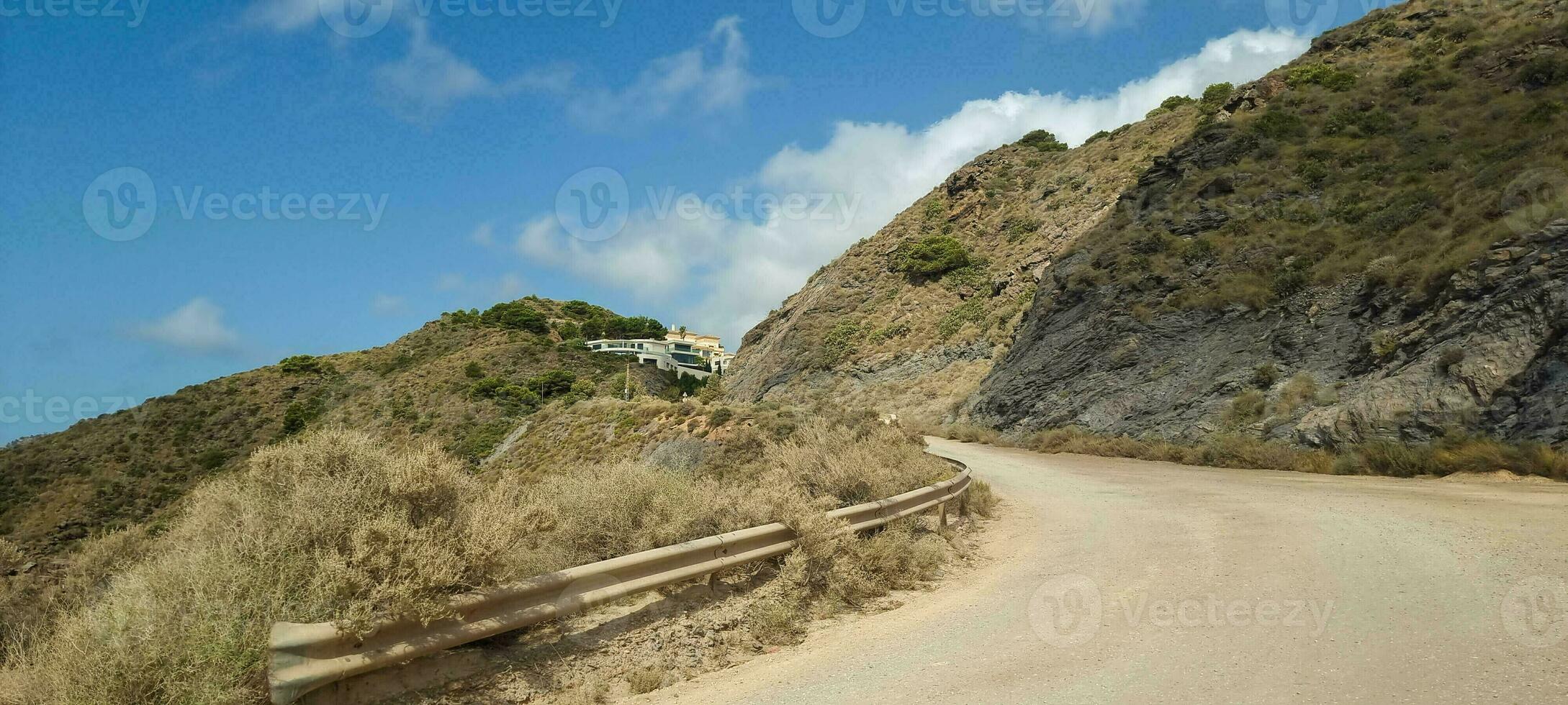 Winding road leading up a hill with sparse vegetation under a clear blue sky. photo
