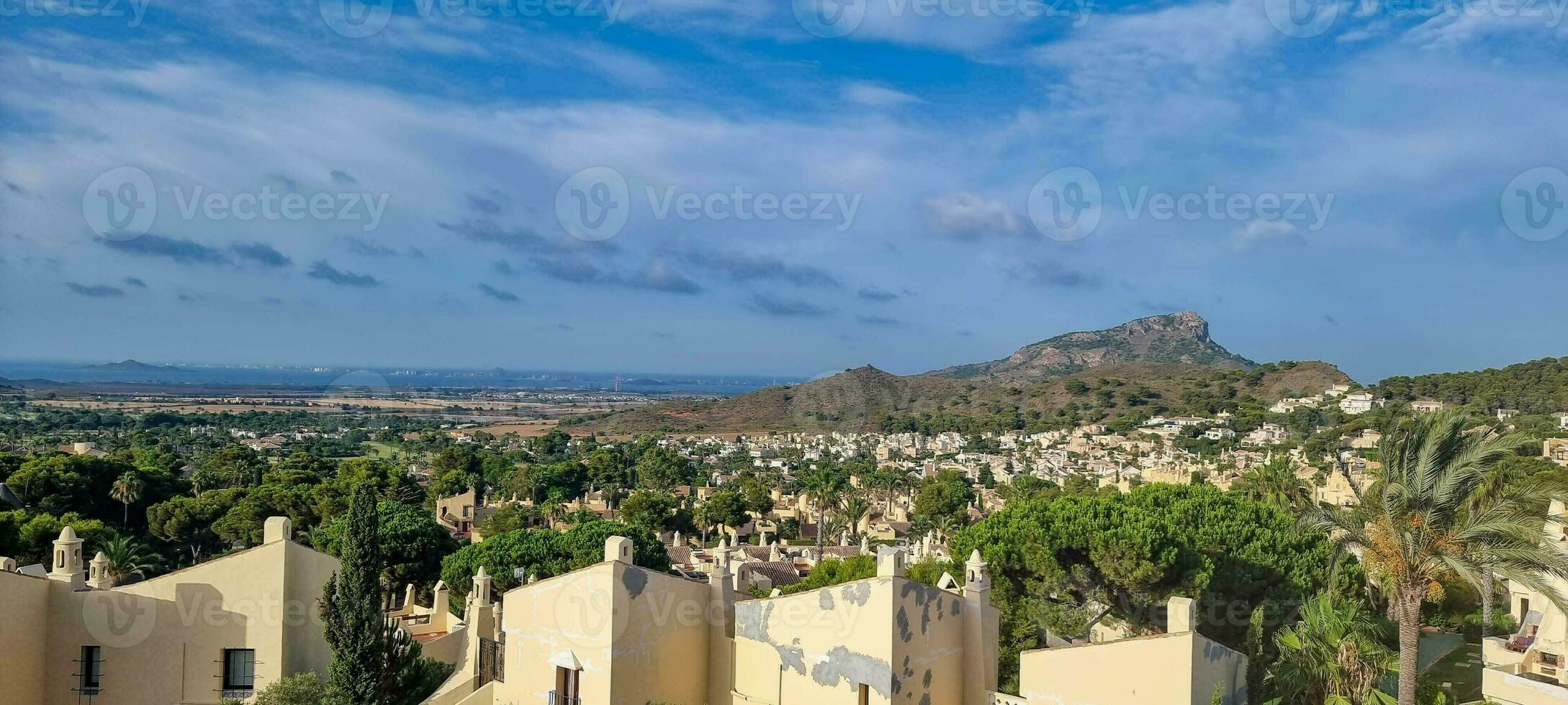 Panoramic view of a Mediterranean town with houses in the foreground and a mountain in the background under a blue sky. photo