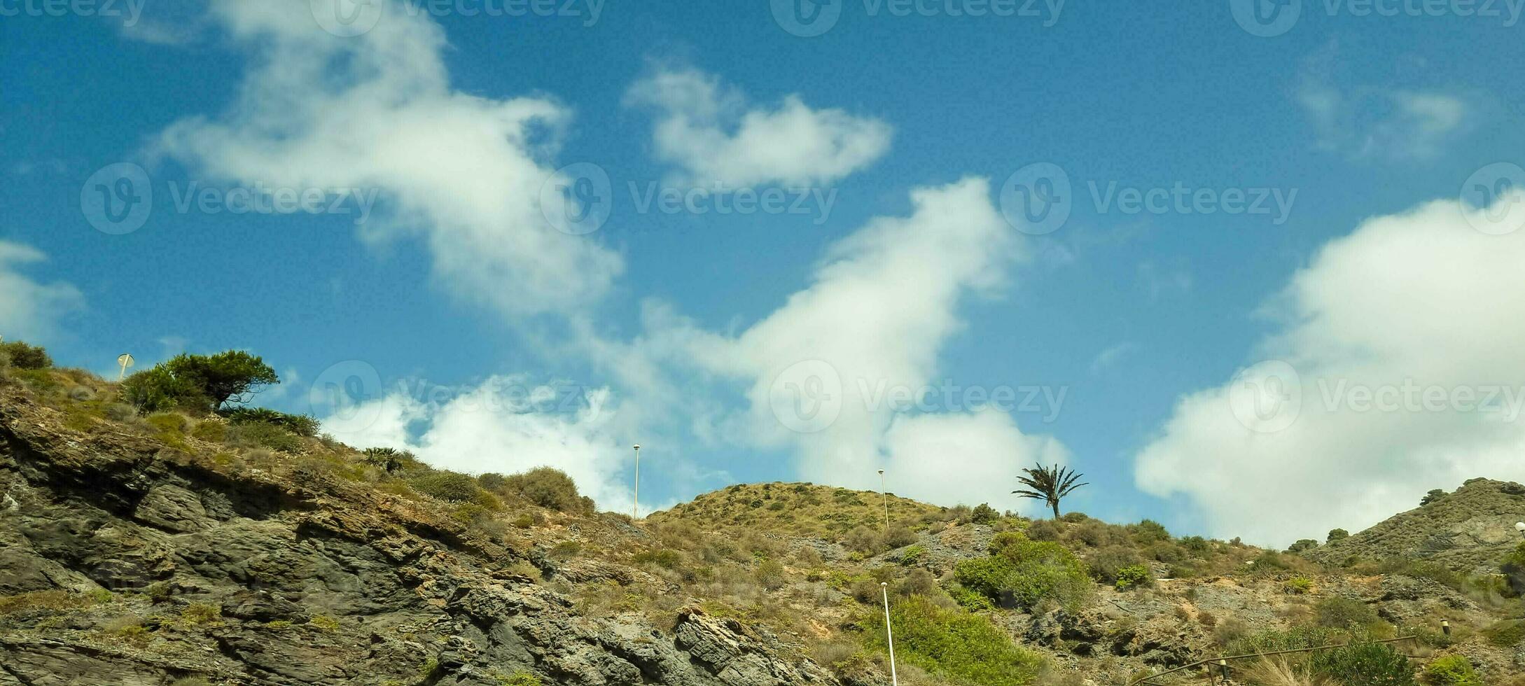 escénico ver de un rocoso ladera con escaso verdor debajo un azul cielo con mullido nubes foto