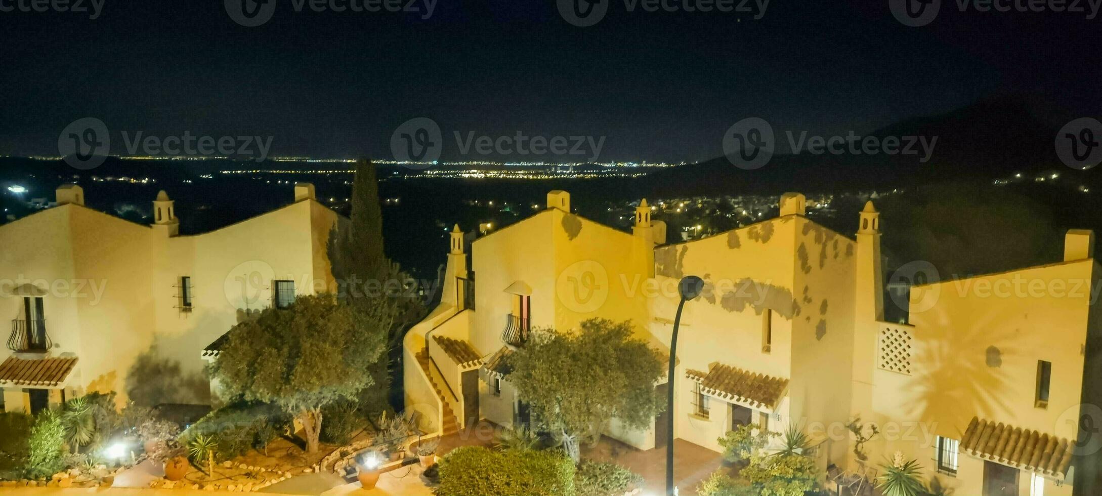 Night view of a traditional village with illuminated buildings against a mountainous backdrop. photo