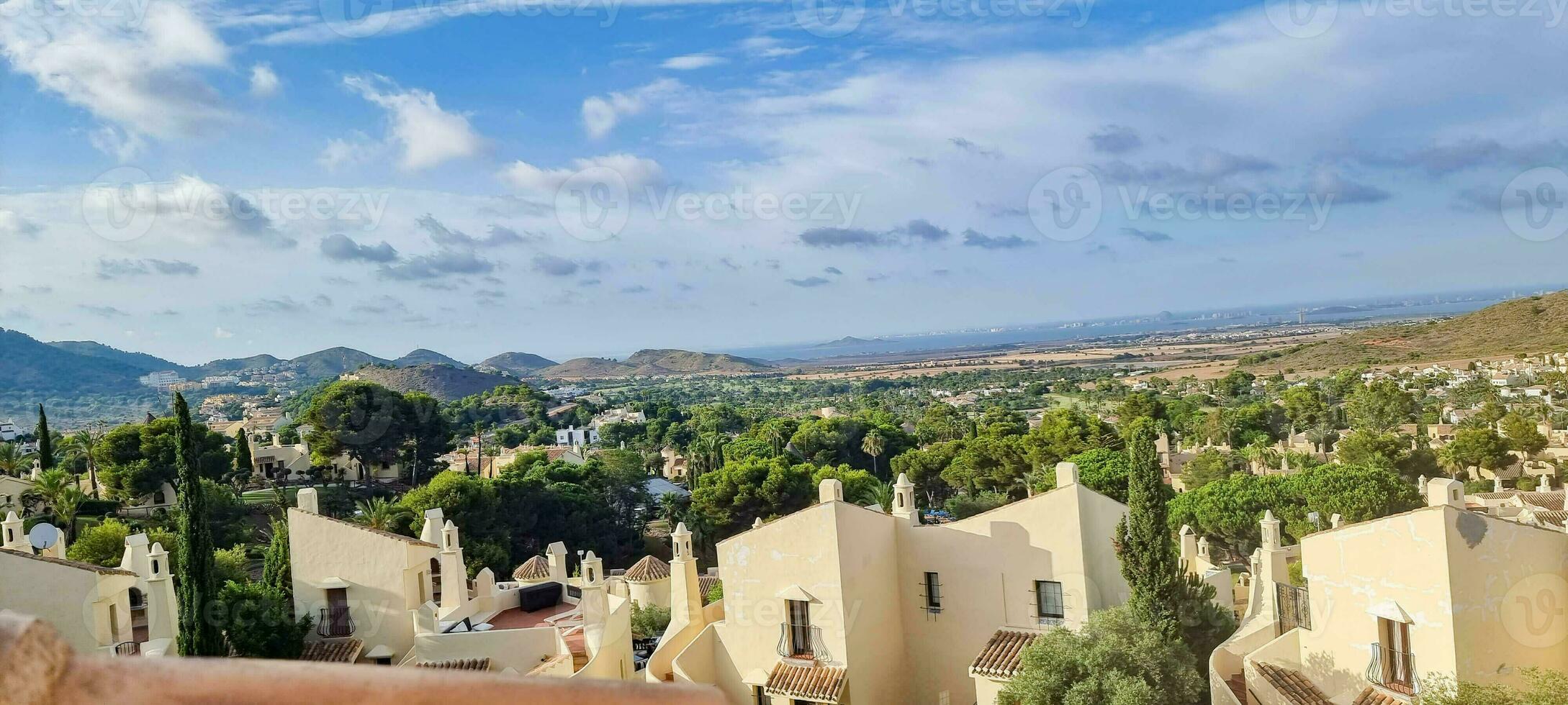 Panoramic view of a Mediterranean town with white houses and greenery under a blue sky with clouds. photo