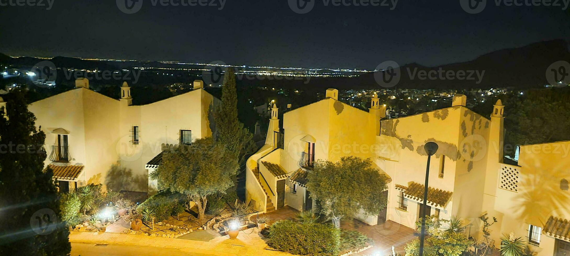 Nighttime view of traditional houses with illuminated streetlights against a mountain backdrop. photo