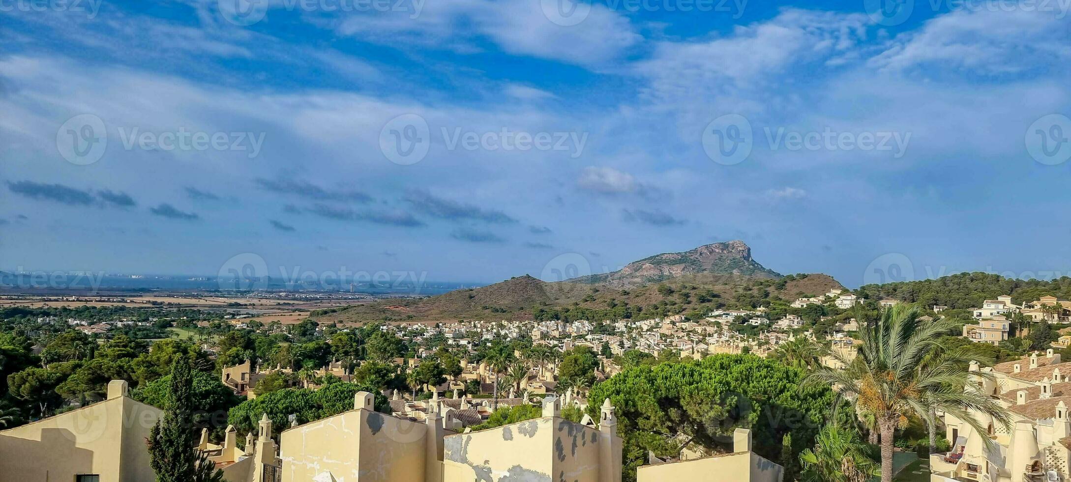 Panoramic view of a Mediterranean landscape with residential buildings in the foreground and mountains in the background under a blue sky. photo