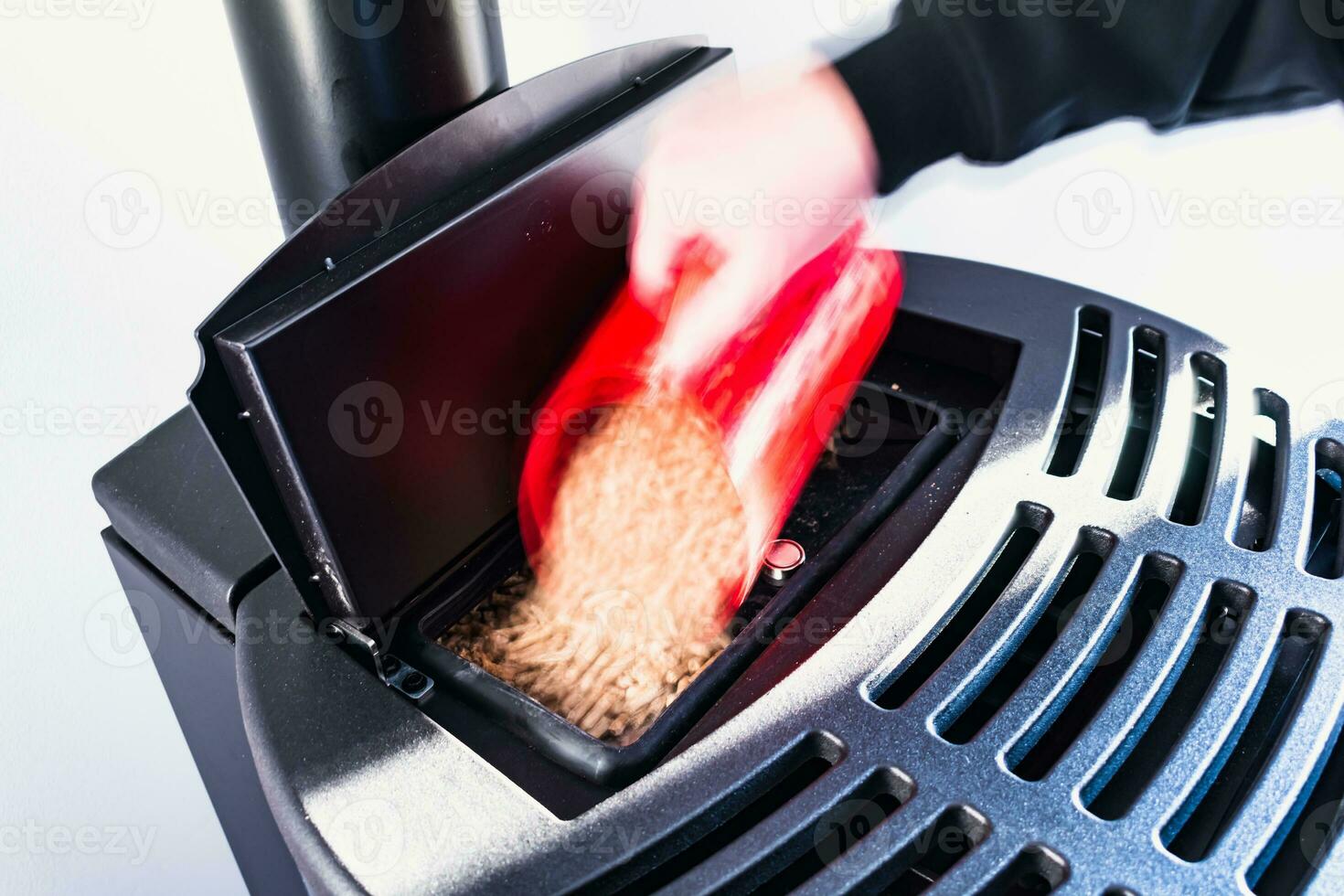 Close-up on pellets, black domestic pellet stove, man loading by hand granules with a red 3 d printed cup photo