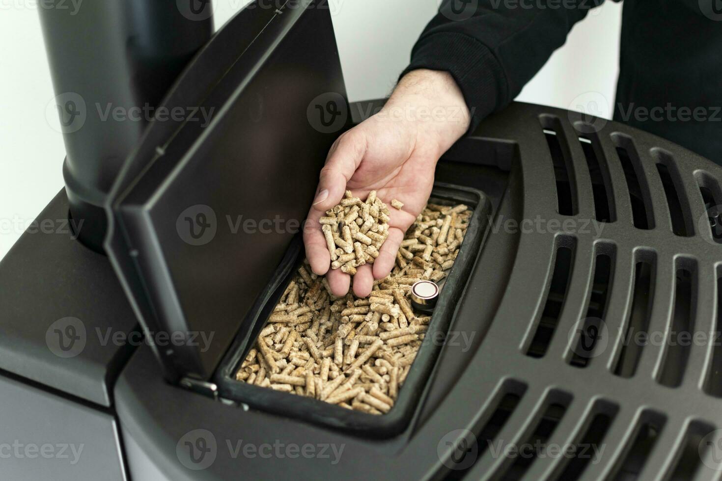 Pellet stove, man holding granules in his hand above a modern black stove photo