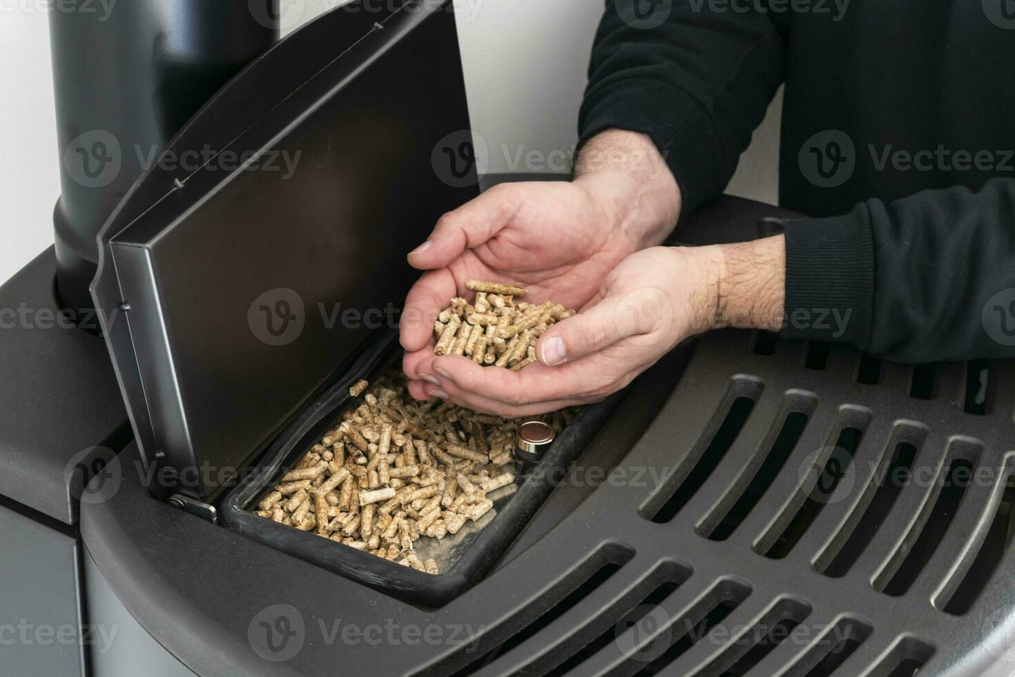 Pellet stove, man holding granules in his hand above a modern black stove photo