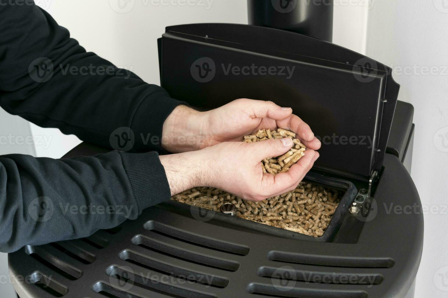 Pellet stove, man holding granules in his hand above a modern black stove photo