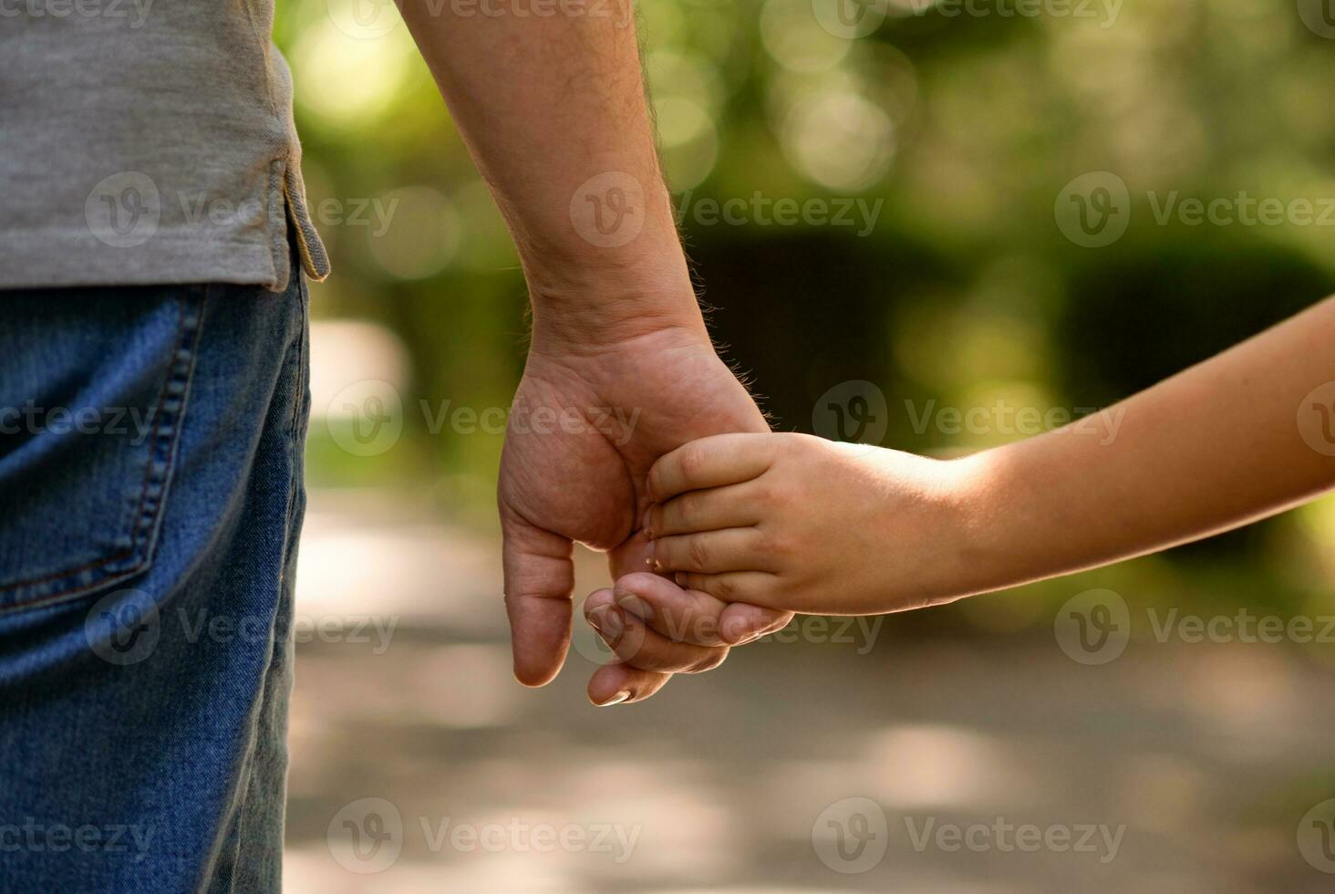 the father's hand held tightly the hand of his little son against the background of green foliage, close-up photo