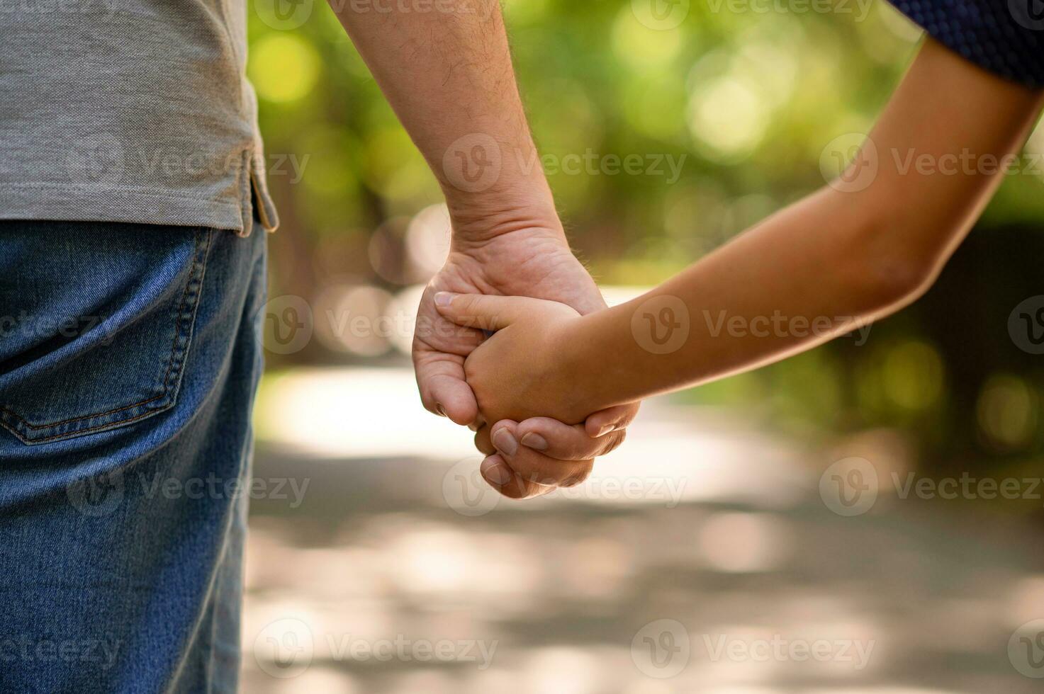 the father's hand held tightly the hand of his little son against the background of green foliage, close-up photo