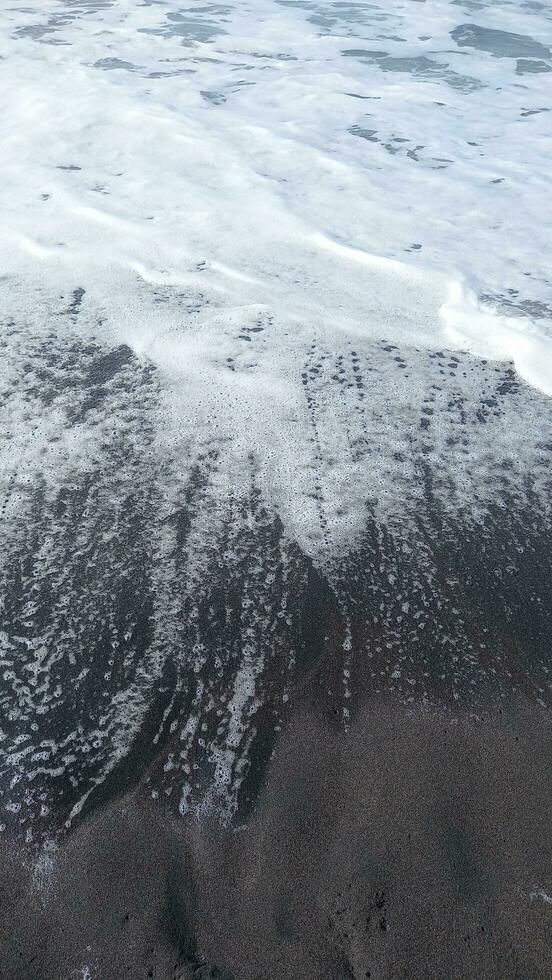 Grey sand beach with water flow. Shoreline high angle view. photo