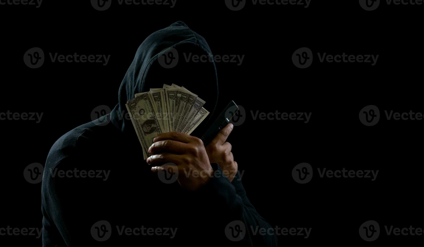 Portrait killer hacker mafia gangster spy man oneperson in black hoodie standing look hand holding money dollar obtained from robbery threat crime attack victim people night dark background copy space photo