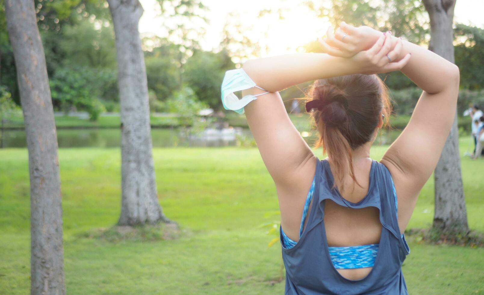 retrato de un hermosa asiático mujer en ropa de deporte, en pie con su atrás, extensión antes de hacer ejercicio al aire libre en el parque en el Mañana a lograr un sano estilo de vida. sano calentamiento arriba foto