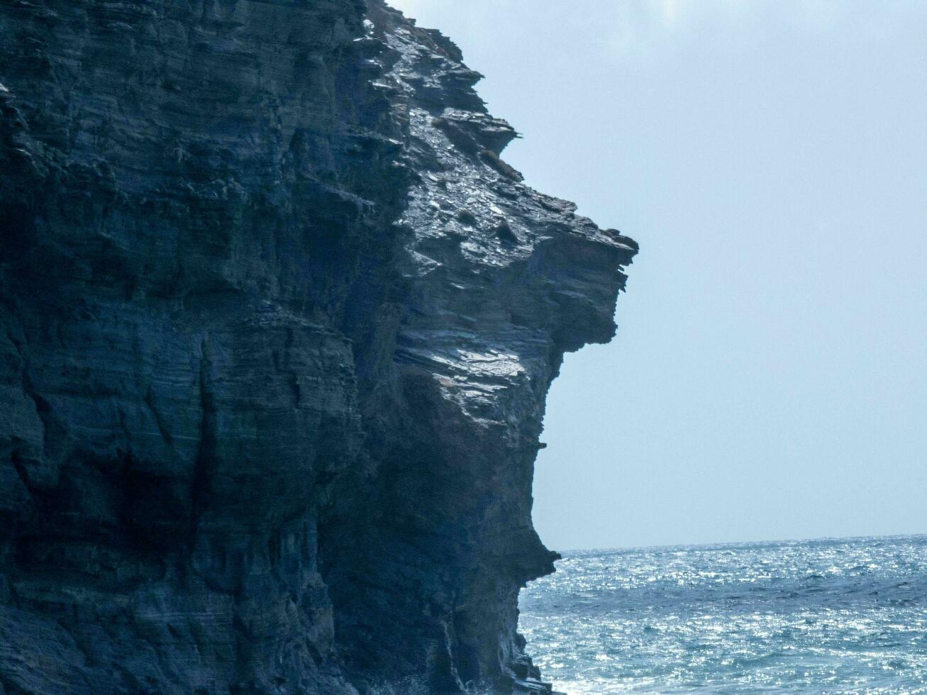 Rock formation resembling a human profile against the ocean background. photo