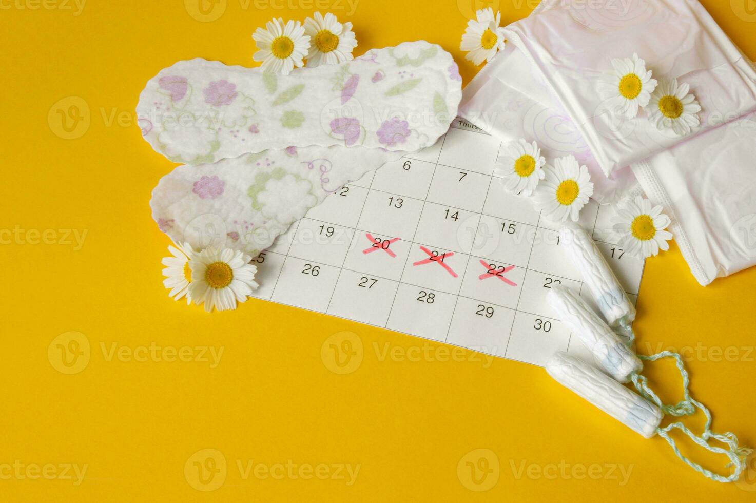 Menstrual pads and tampons on menstruation period calendar with chamomiles on yellow background. photo