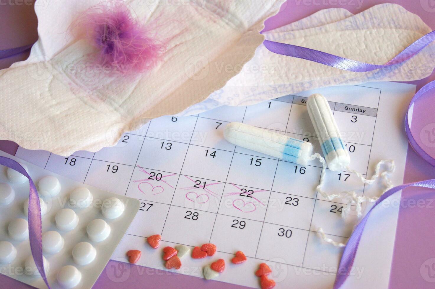 Menstrual pads and tampons on menstruation period calendar with on lilac background. photo