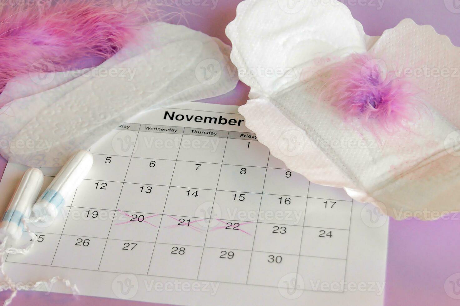 Menstrual pads and tampons on menstruation period calendar with on lilac background. photo