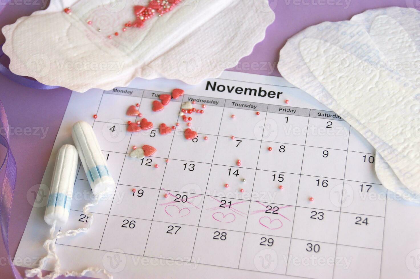 Menstrual pads and tampons on menstruation period calendar with on lilac background. photo