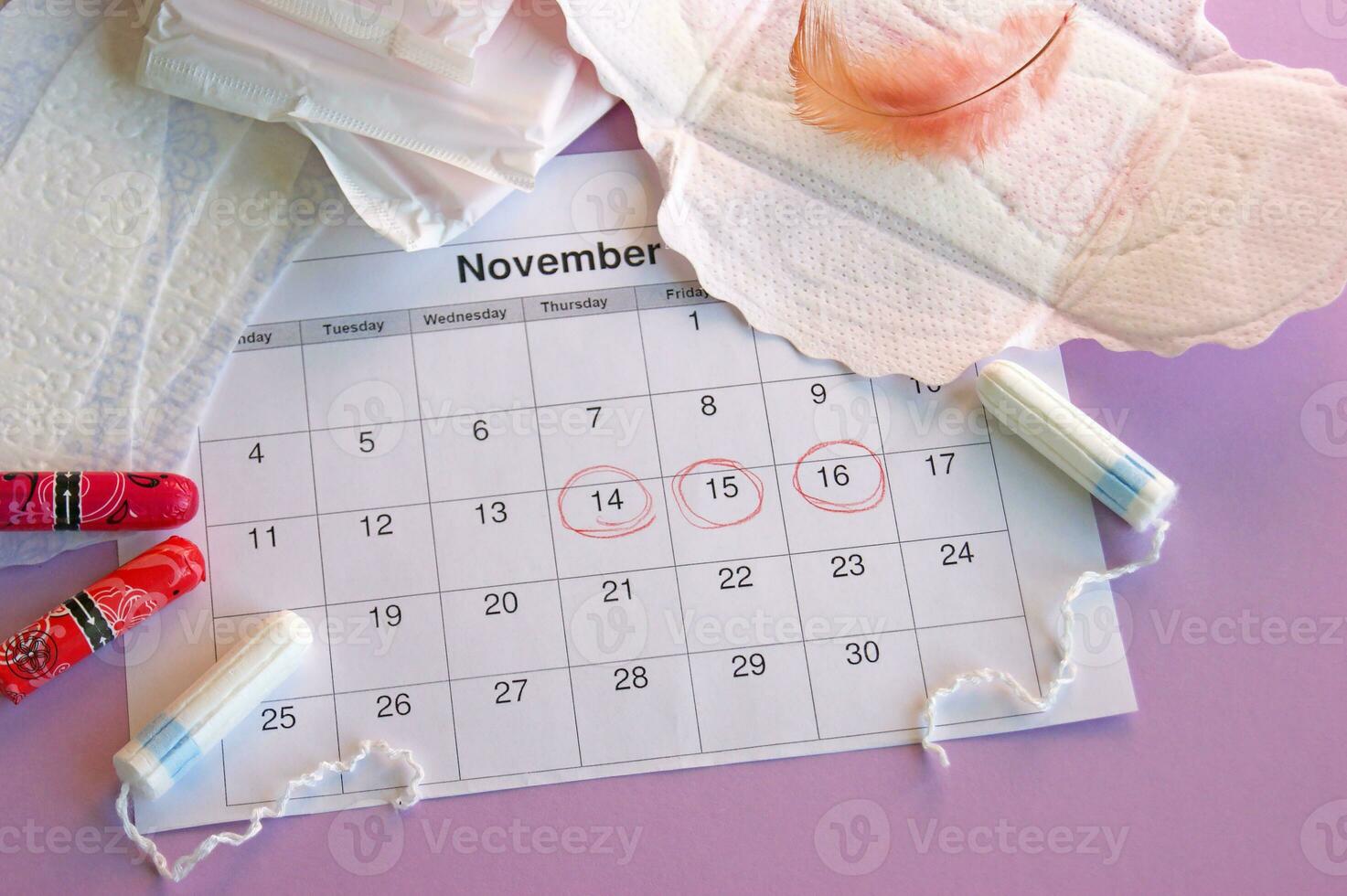Menstrual pads and tampons on menstruation period calendar with on lilac background. photo