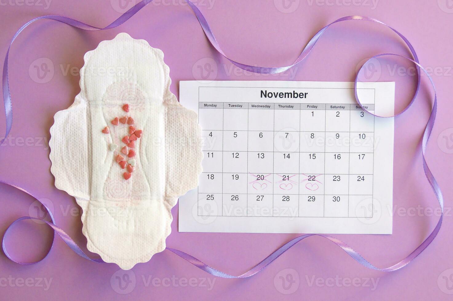 Menstrual pads and tampons on menstruation period calendar with on lilac background. photo