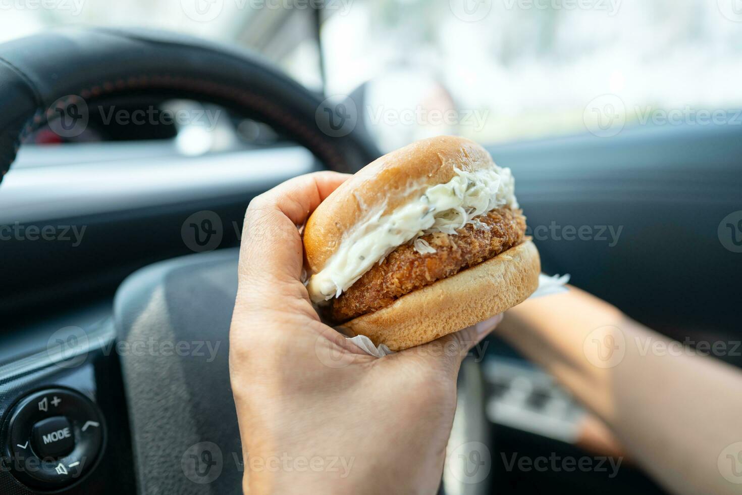 Asian lady holding hamburger to eat in car, dangerous and risk an accident. photo