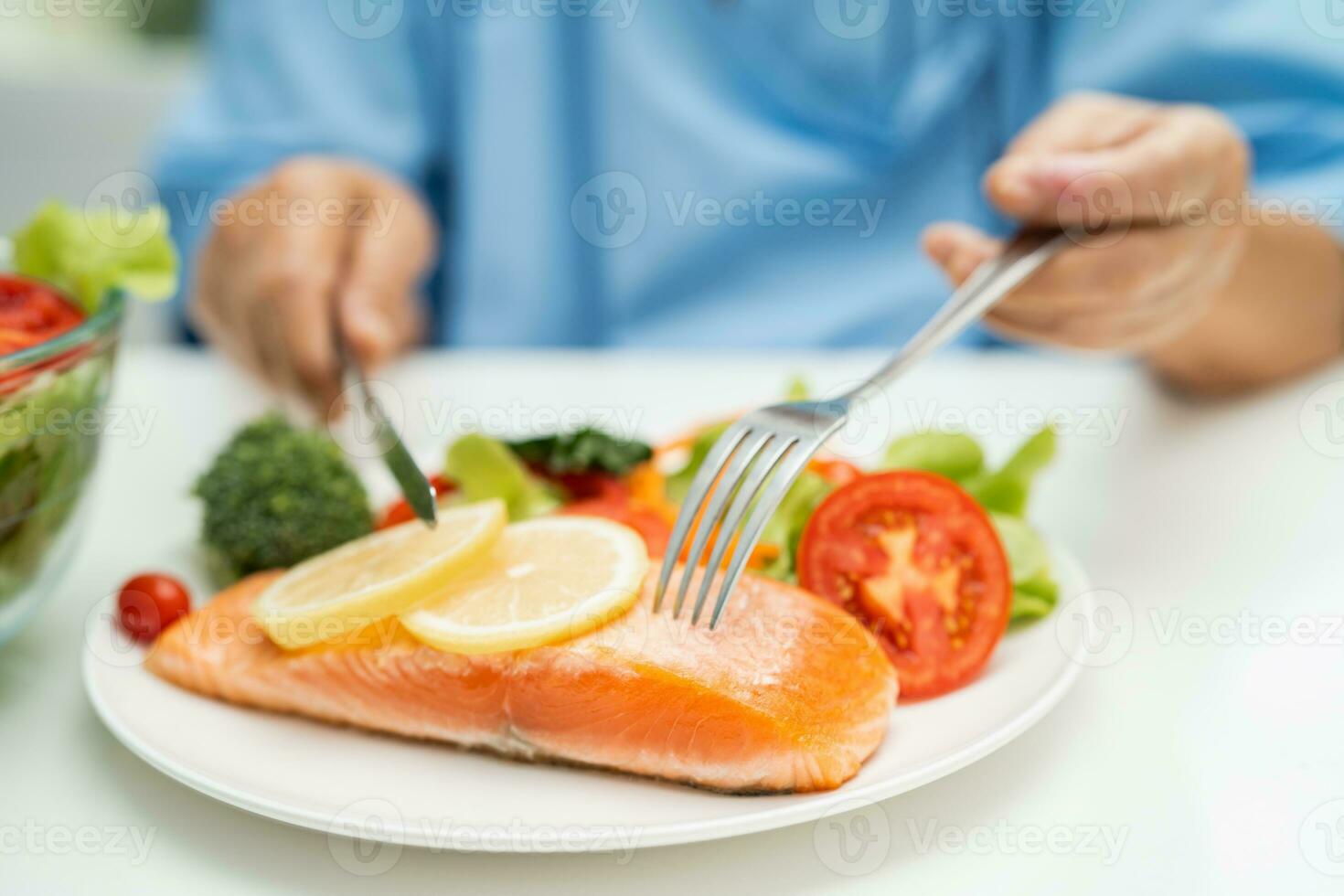 Asian elderly woman patient eating salmon steak breakfast with vegetable healthy food in hospital. photo