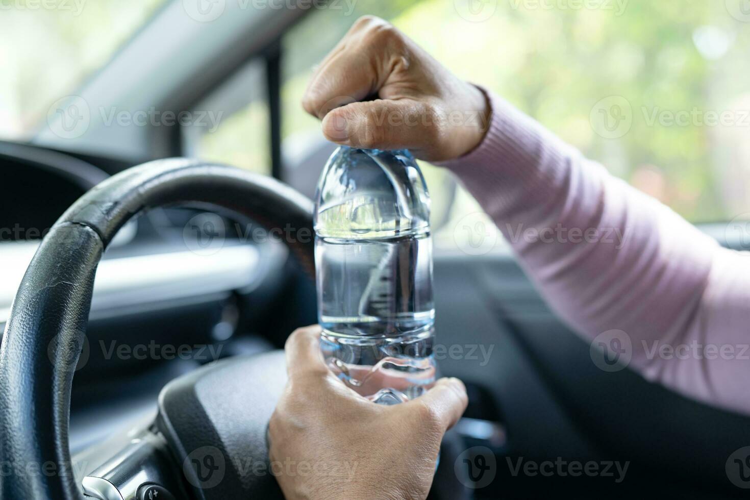 Asian woman driver holding bottle for drink water while driving a car. Plastic hot water bottle cause fire. photo