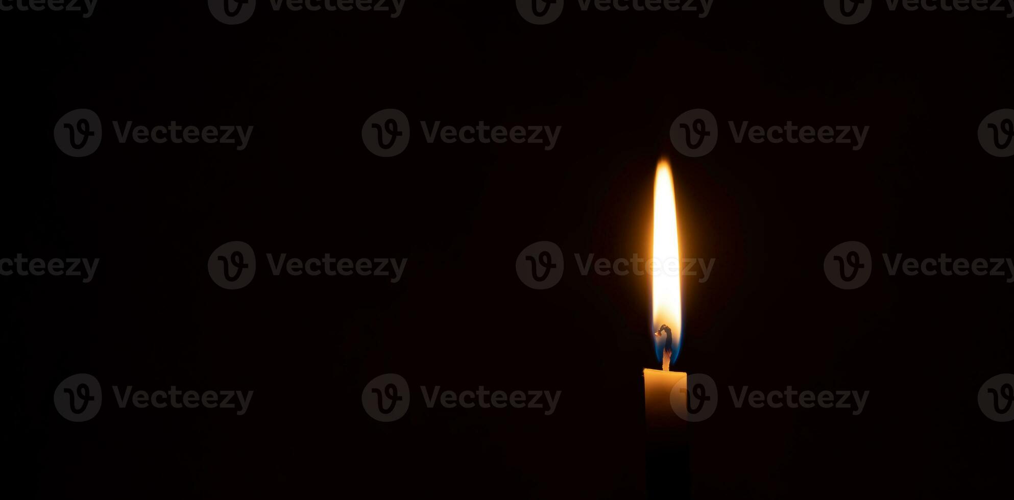 A single burning candle flame or light glowing on a small orange candle on black or dark background on table in church for Christmas, funeral or memorial service with copy space photo