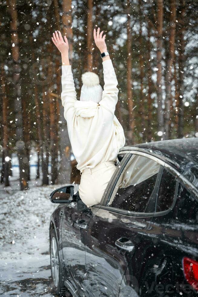 Young woman in woolen white hat have a fun in the car. Winter travel in the forest. Snowy weather. . High quality photo