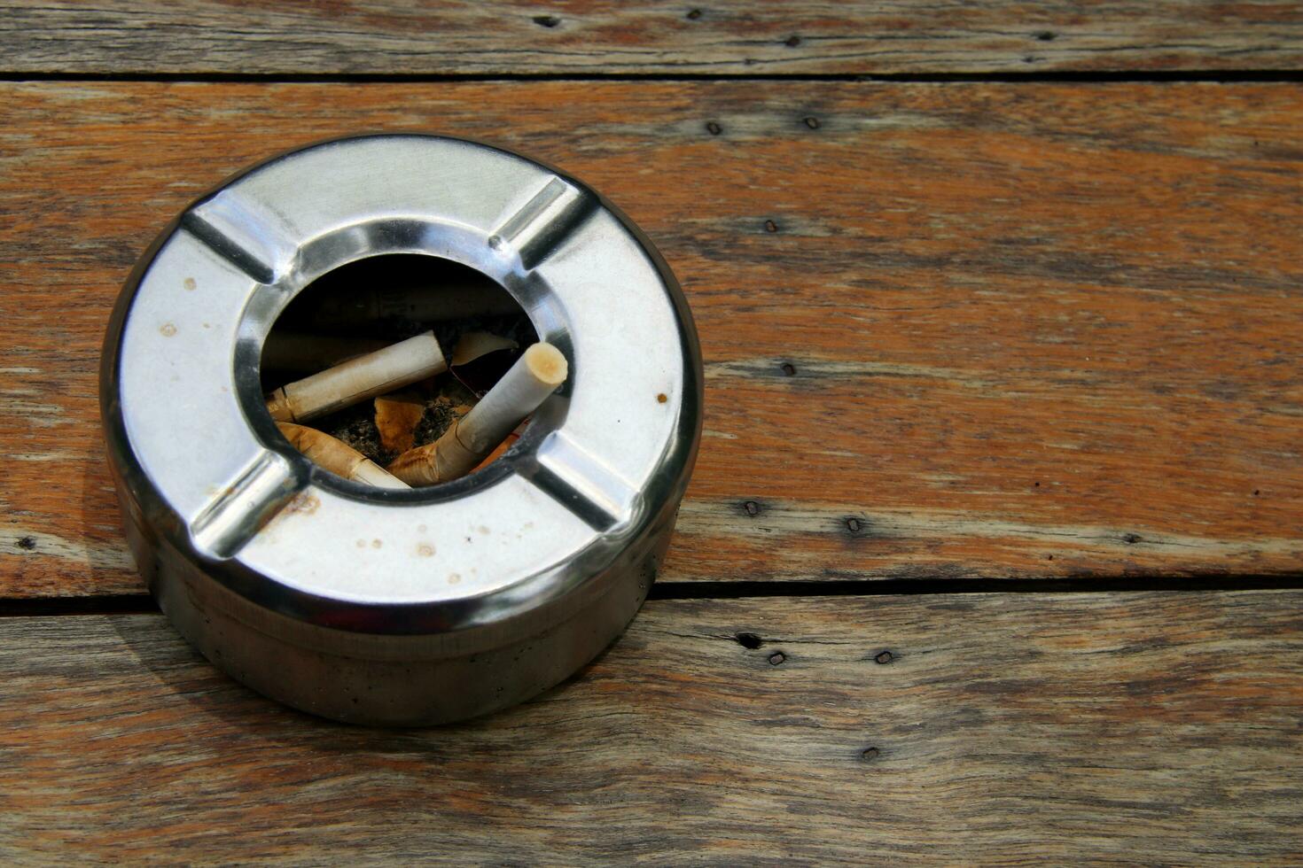 Round shape stainless ashtray on old brown wood plank and tobacco, Thailand. photo