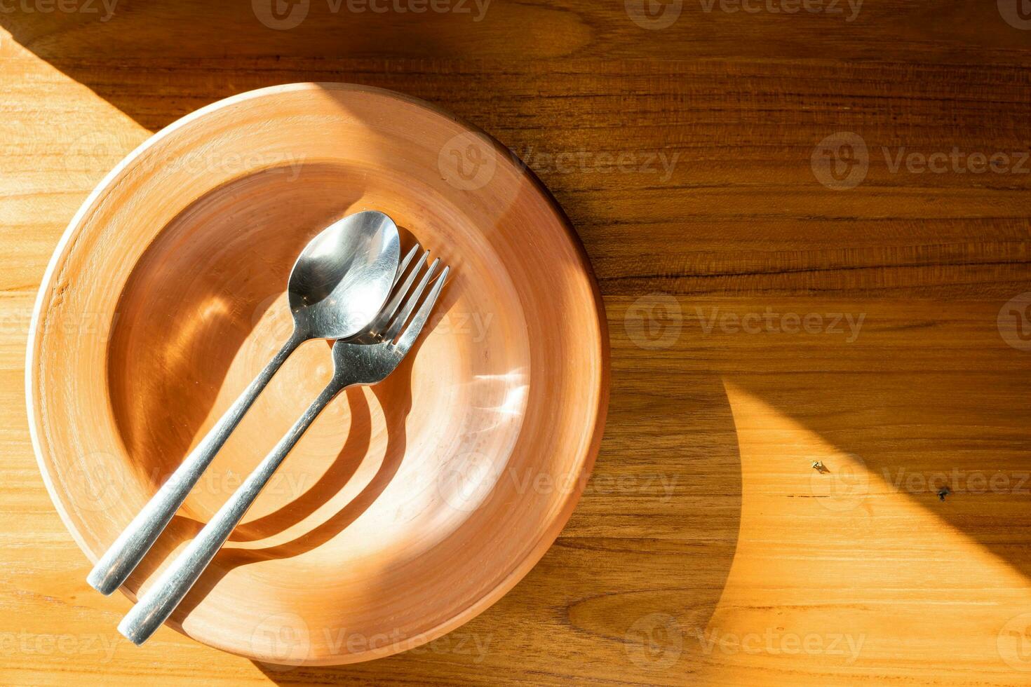 Close up stainless steel cutlery on clay plate. Clay Plate with spoon and fork on wooden table with sunlight. photo