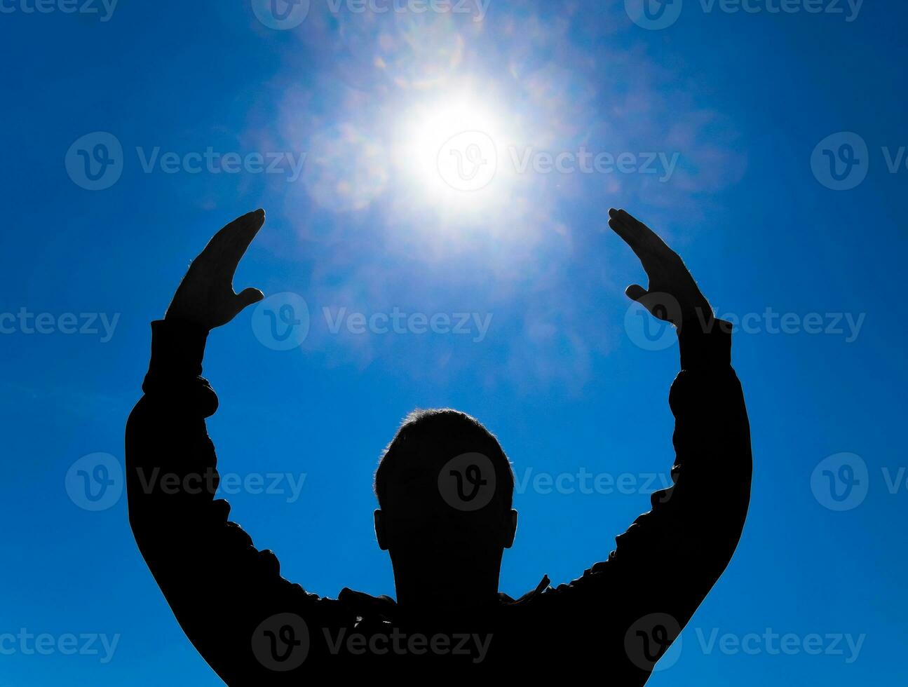 Silhouette of a man against the background of the sun and blue sky. Hands are raised up to the sun photo