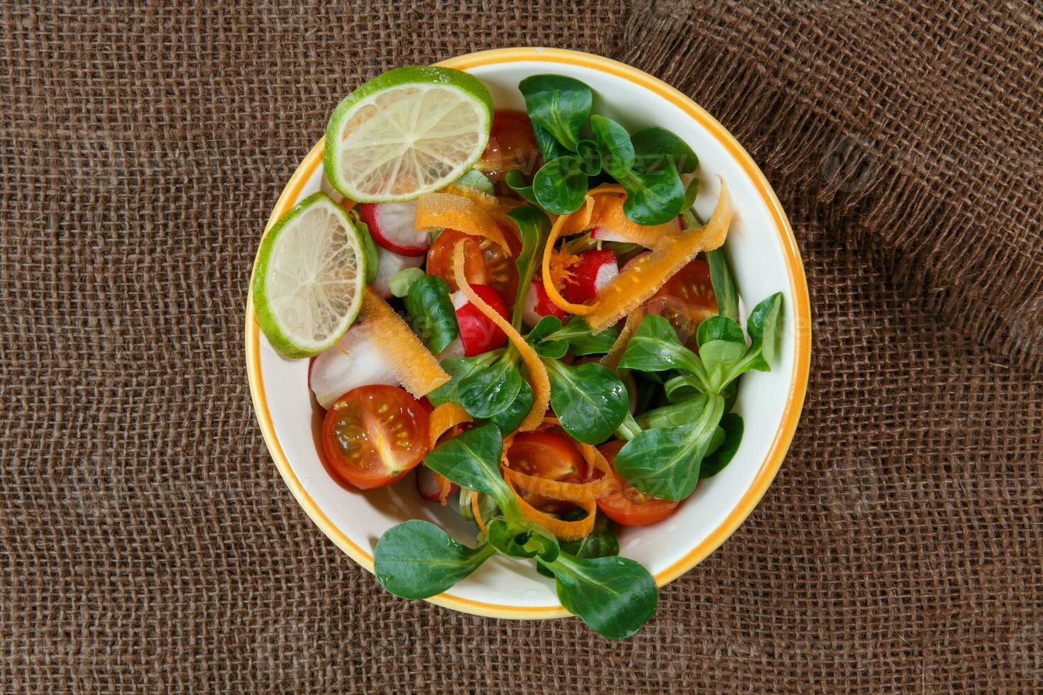 Bowl of fresh vegetable salad on jute table cloth photo