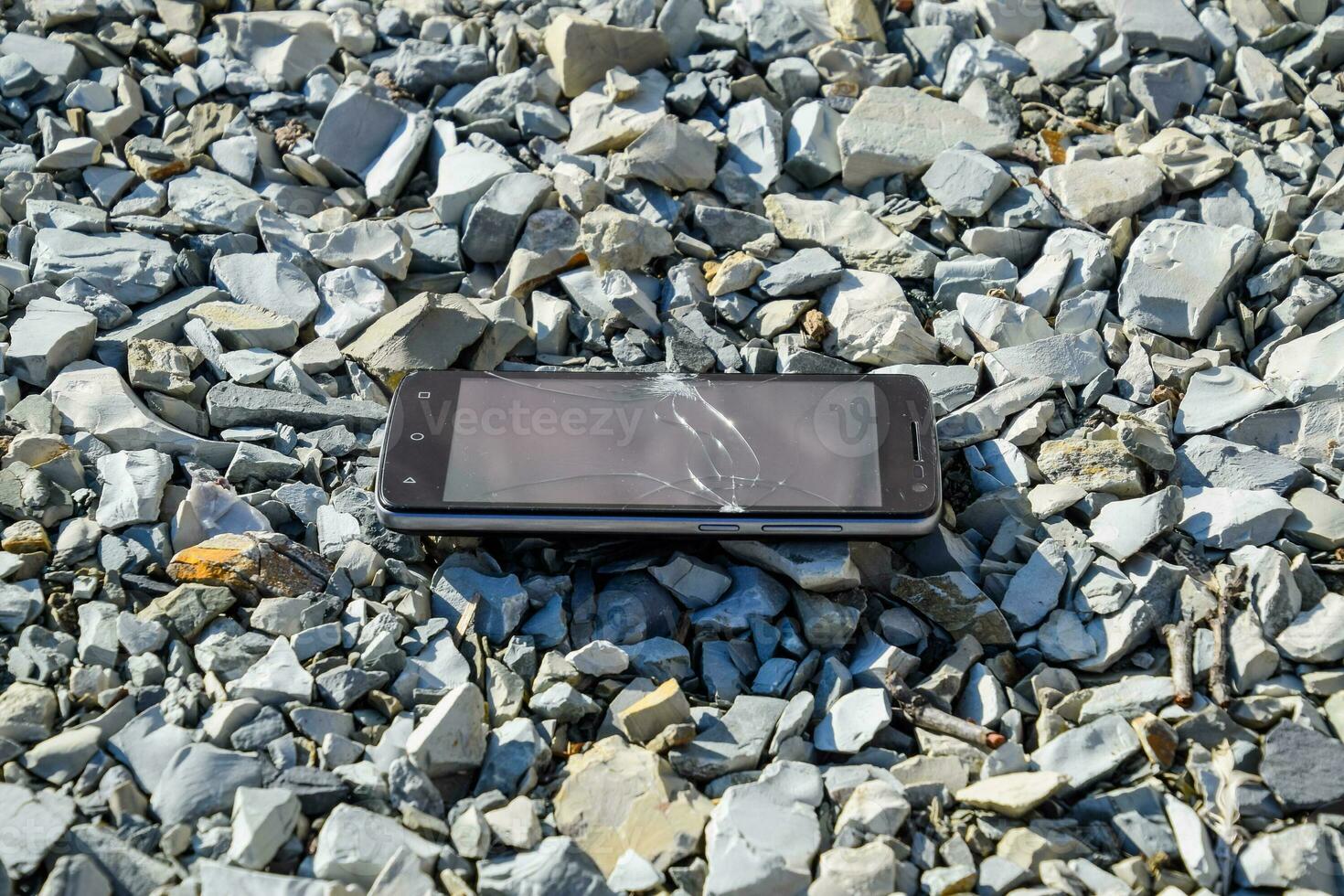 Frustrated phone on the rocks. Glass shattered on rocks on a sma photo