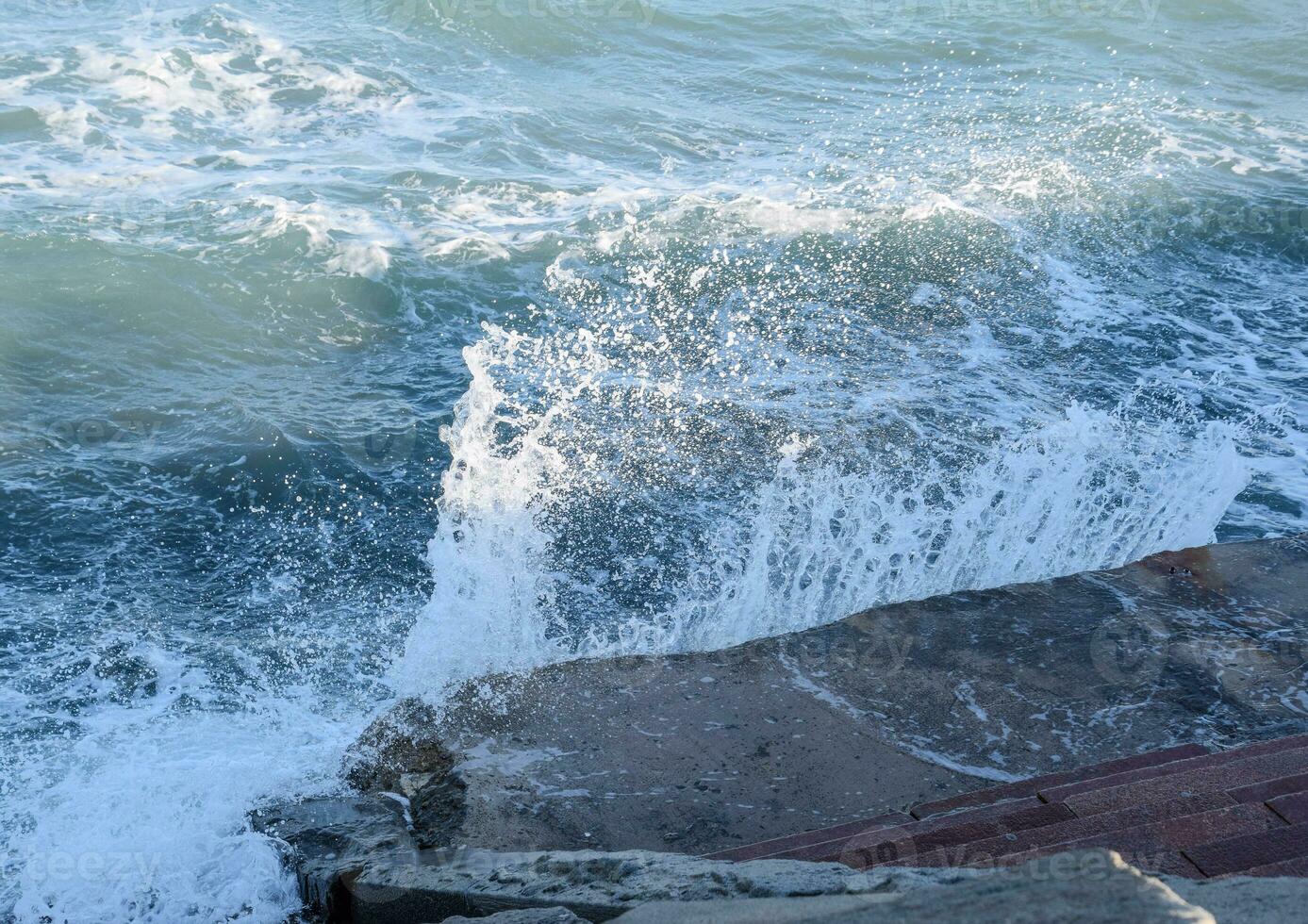 Splashes of waves on the concrete beachfront promenade. Stone steps to the sea photo