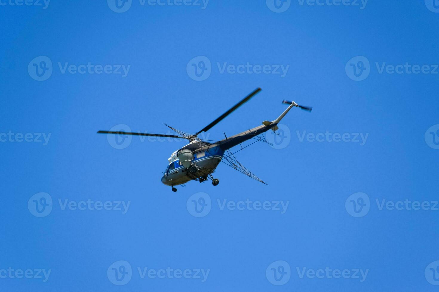 A helicopter of agricultural aviation is flying in the blue sky. photo