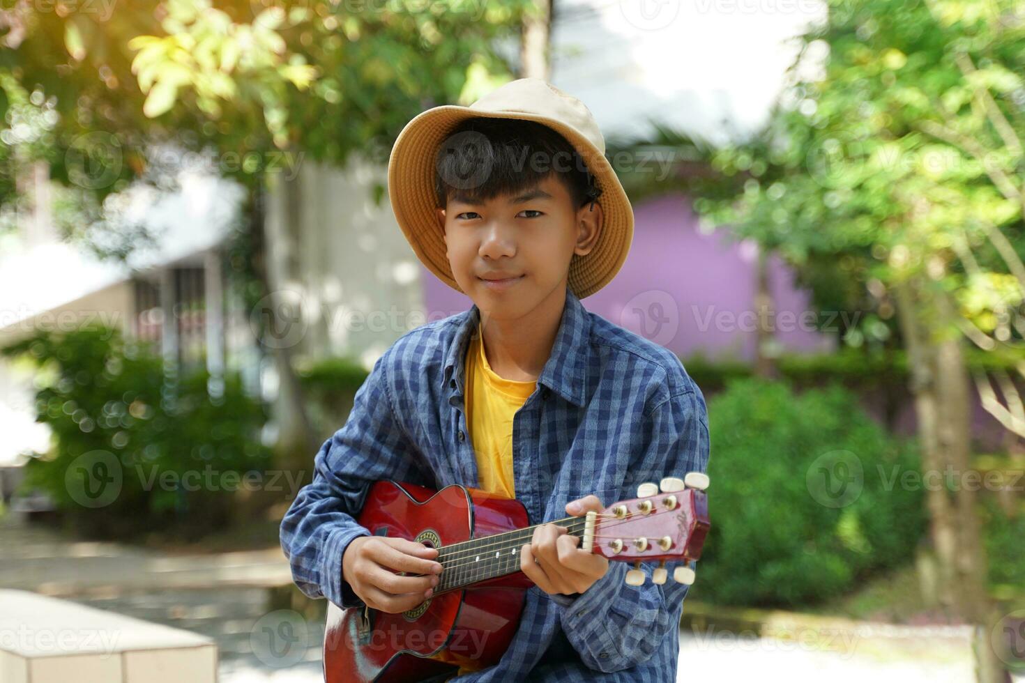 An Asian boy plays the ukulele during his free time in the school yard under the trees. Soft and selective focus. photo