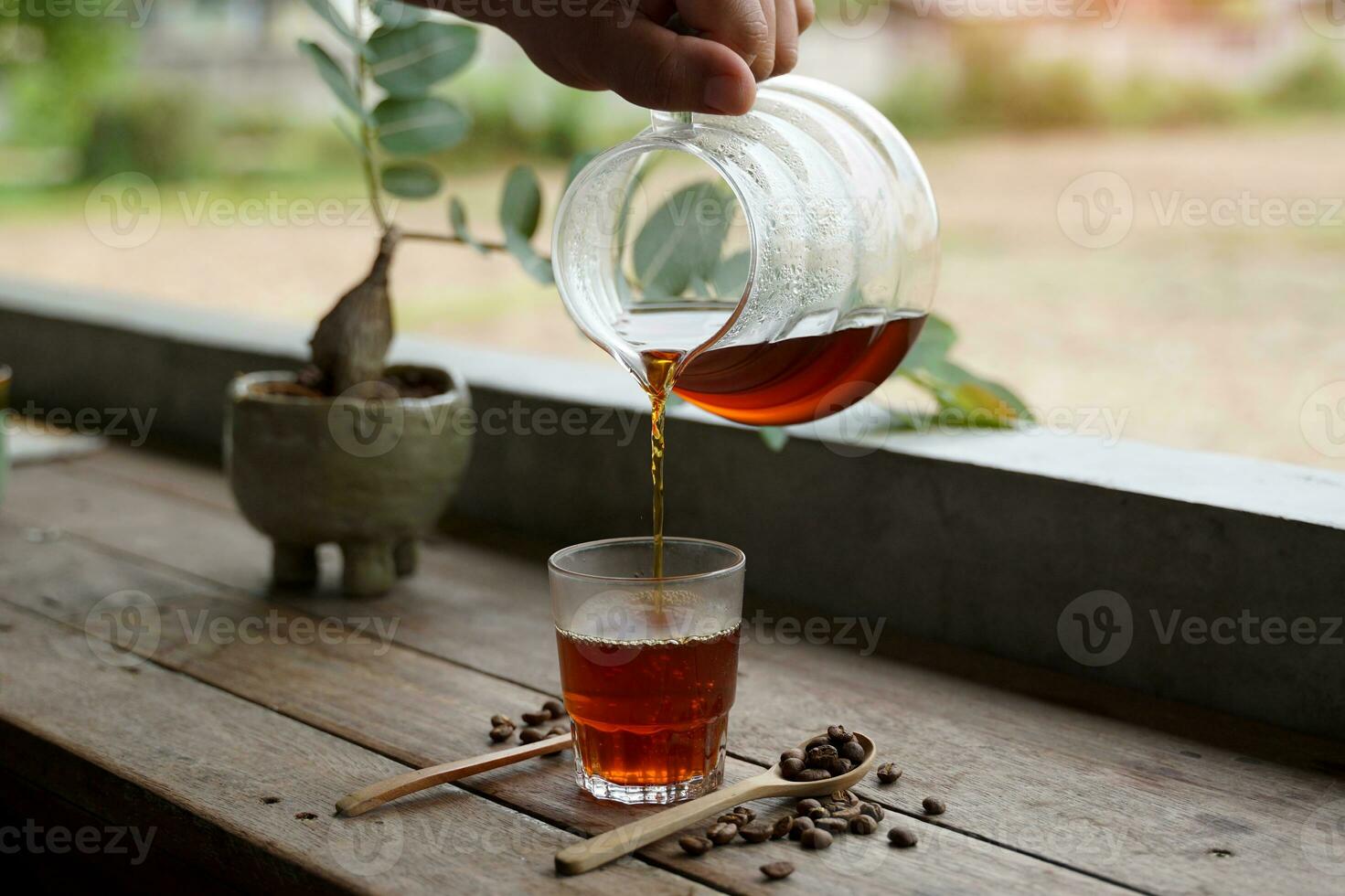 Holding a glass carafe, pour the black drip coffee into the cup and serve it in the morning. photo