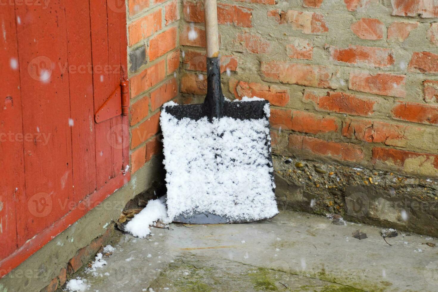 A snow shovel in the snow and stands in the corner photo